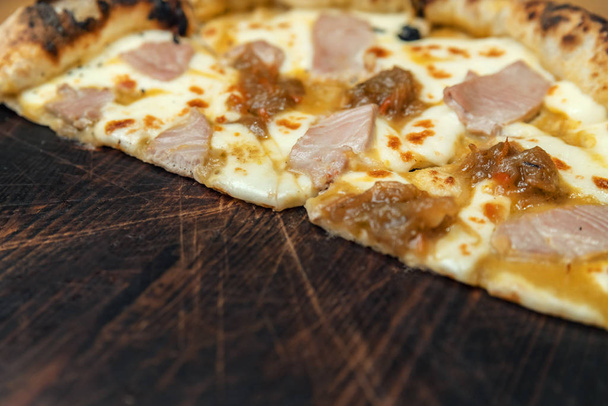 Hot pizza slice with melting cheese on a rustic wooden table. - Фото, изображение