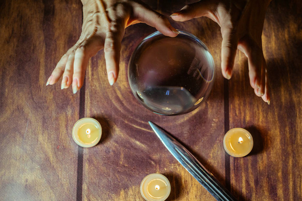 Magiczna kryształowa kula, nóż, świece i ręce wróżki lub czarownicy manipulującej piłką - Zdjęcie, obraz
