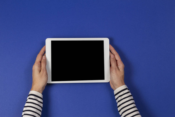 Female hands holding digital tablet computer on navy blue background. Top view - Фото, изображение