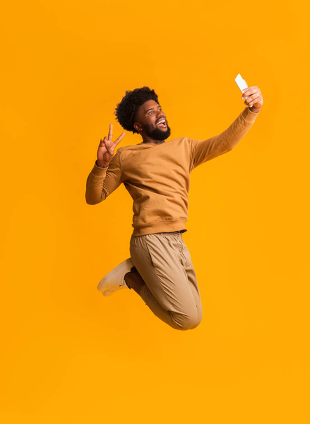 zwart emotionele guy het nemen van selfie terwijl springen - Foto, afbeelding