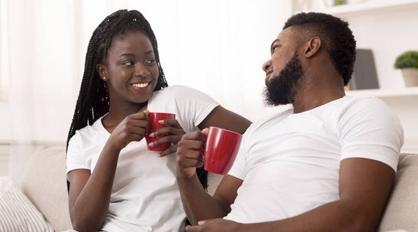 若いアフリカ系アメリカ人のカップルが自宅でリラックスし、コーヒーを飲み、チャット - 写真・画像