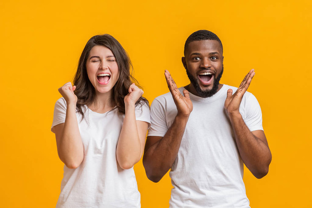 Interracial couple rejoicing success, emotionally celebrating good news over yellow background - Fotó, kép