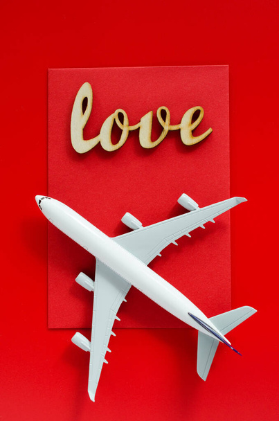 Προγραμματισμός ταξιδιού την ημέρα του Αγίου Βαλεντίνου. Ταξιδιωτική ιδέα. Επιγραφή αγάπη και το μοντέλο του επιβατικού αεροπλάνου σε κόκκινο φόντο. - Φωτογραφία, εικόνα