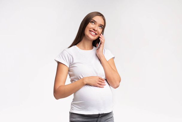 Mosolygó terhes nő beszél mobilon keresztül fehér stúdió háttér - Fotó, kép