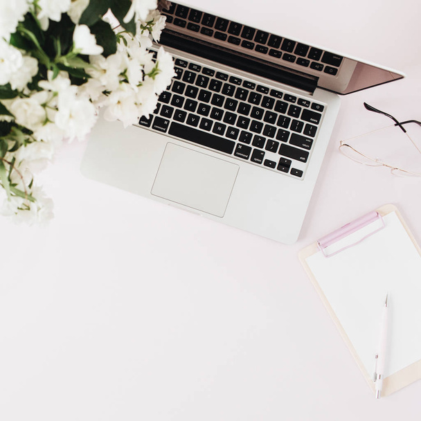 Office desk workspace with laptop, flowers bouquet, clipboard on pink table. Flat lat, top view. - Φωτογραφία, εικόνα