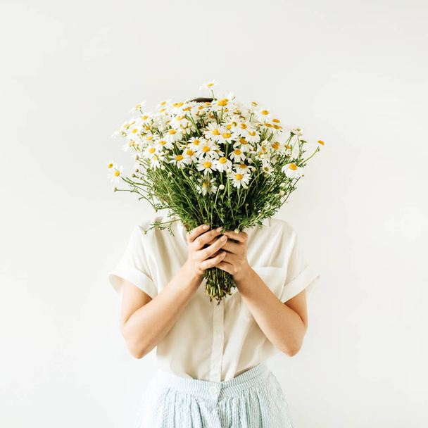 Young pretty woman with bouquet of white chamomile daisy flowers on white background. - Foto, afbeelding