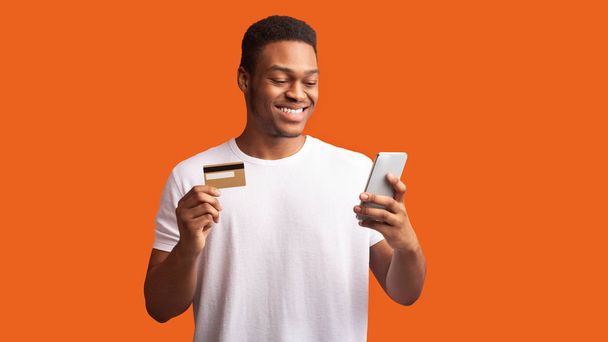 Black guy holding credit card and smartphone - Zdjęcie, obraz
