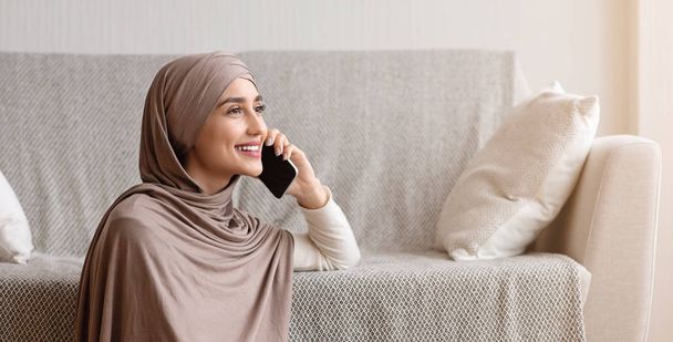 Başörtülü genç Arap kız evde cep telefonuyla konuşuyor. - Fotoğraf, Görsel