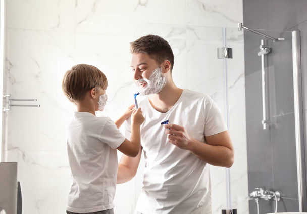 Dad and son with shaving foam on their faces having fun in bathr - Фото, изображение