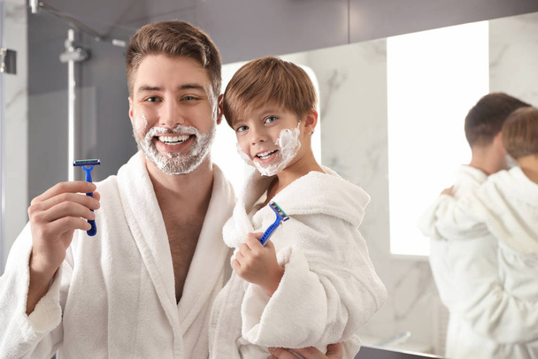 Dad and son with shaving foam on faces holding razors in bathroo - 写真・画像