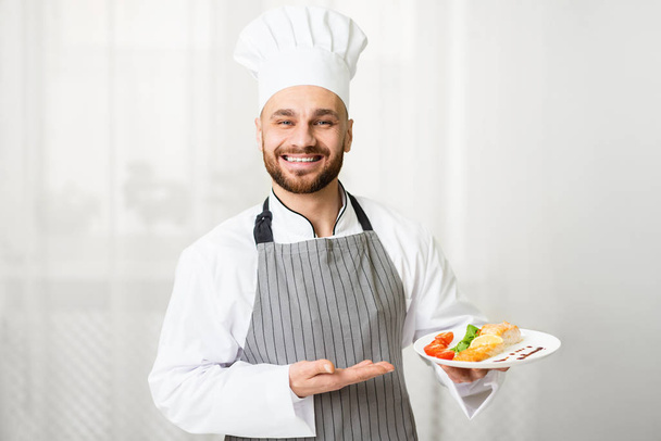 Chef sosteniendo la placa con filete de salmón asado de pie en la cocina
 - Foto, imagen