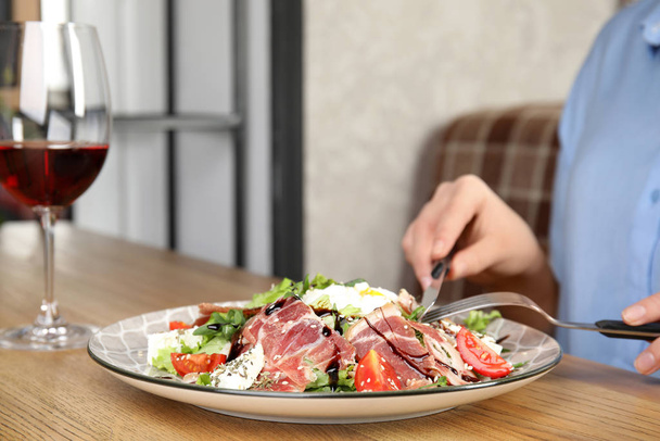 Woman eating delicious prosciutto salad at wooden table indoors, closeup. Space for text - 写真・画像