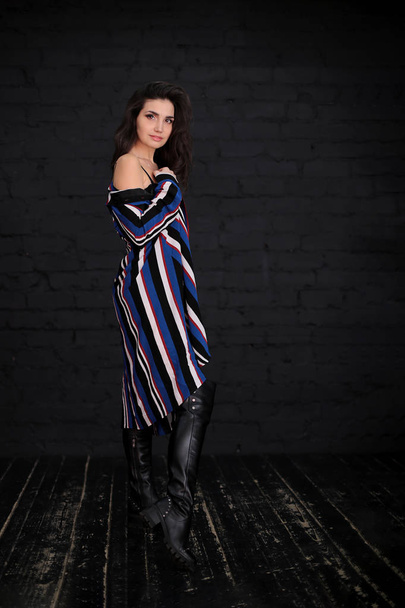 retrato de una hermosa joven con cabello oscuro en un body negro y un cárdigan rayado sobre las botas de rodilla sobre un fondo oscuro
 - Foto, Imagen