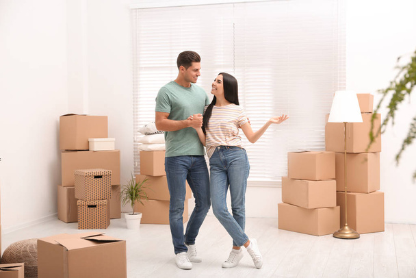 Happy couple in room with cardboard boxes on moving day - Фото, изображение