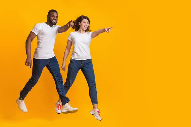 Saltar pareja interracial apuntando al espacio de copia sobre fondo amarillo
 - Foto, imagen