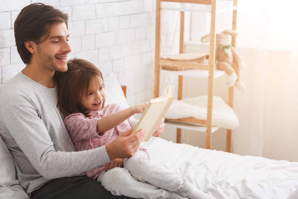 Little daughter and father enjoying book, spending weekend together - Foto, imagen