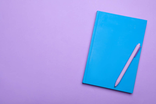 Light blue notebook and pen on lilac background, top view. Space for text - Fotografie, Obrázek