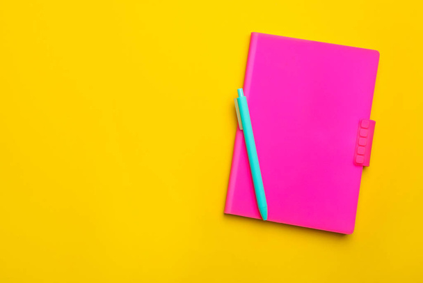 Cuaderno rosa y bolígrafo sobre fondo amarillo, vista superior. Espacio para texto
 - Foto, imagen
