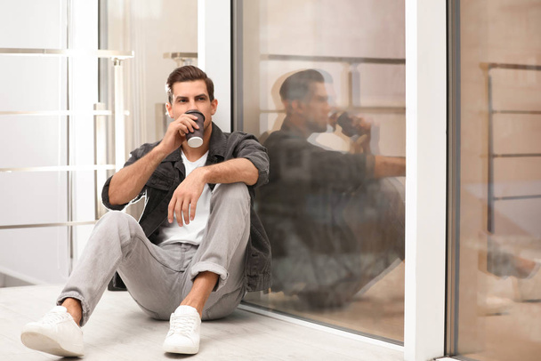 Handsome man drinking coffee near window at home - Zdjęcie, obraz
