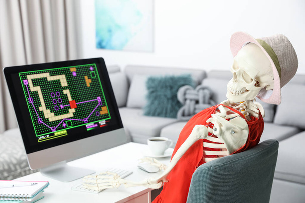 Human skeleton in red dress playing game at home - Foto, afbeelding