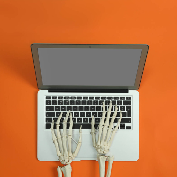 Human skeleton using laptop on orange background, top view - Фото, изображение