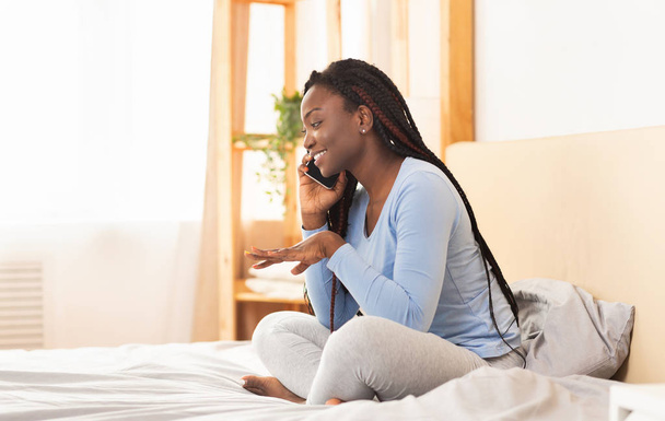 Afro Girl hablando por celular sentado en la cama en el dormitorio
 - Foto, imagen