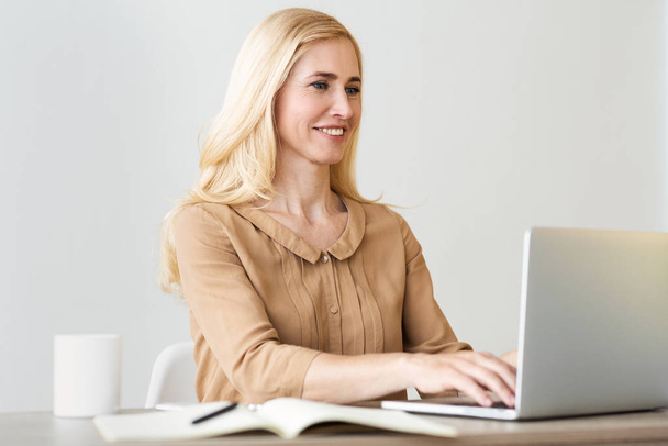 Жінка-підприємець. Бізнес-леді середнього віку друкують на ноутбуці
 - Фото, зображення