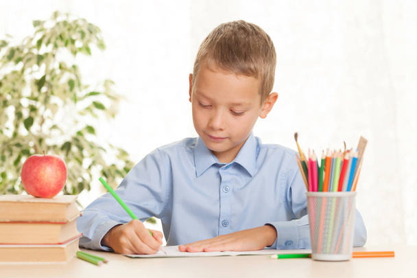 Fiatal iskolás fiú ül az asztalnál, és házi feladatot csinál. Az alapfokú oktatás fogalma - Fotó, kép