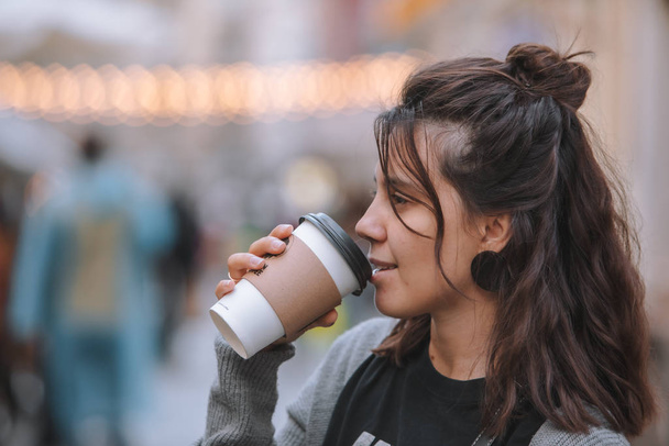 молодая красивая женщина на городской улице пьет кофе из одноразовой чашки
 - Фото, изображение