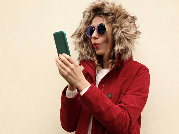 Portrait surprised woman holding phone wearing red jacket with h - Valokuva, kuva
