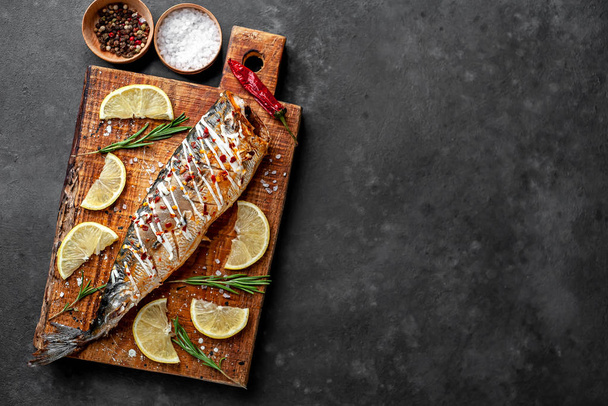 Baked mackerel with lemon and spices served on wooden board - Photo, Image