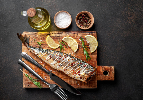 Baked mackerel with lemon and cutlery served on wooden board - Photo, Image