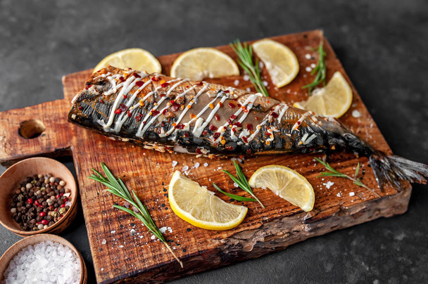 Baked mackerel with lemon and spices served on wooden board - Фото, изображение