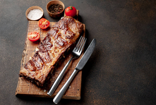 Côtes de porc grillées entières avec tomates, couverts et épices sur planche de bois
 - Photo, image