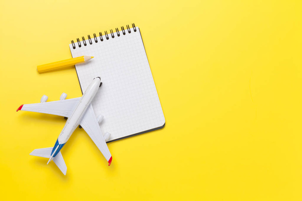Travel concept with notepad for your plan list and airplane toy over yellow sunny backdrop. Top view flat lay with copy space - Foto, Imagen