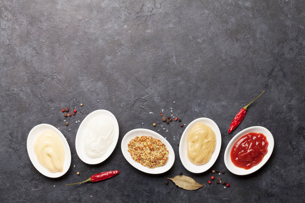 Zestaw różnych sosów. Popularne sosy w misach - ketchup, musztarda, majonez na ciemnym kamiennym stole. Widok z góry z miejsca kopiowania. Układy płaskie - Zdjęcie, obraz