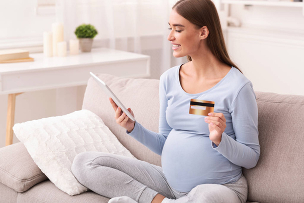 Mujer embarazada usando tableta digital y tarjeta de crédito en casa
 - Foto, imagen