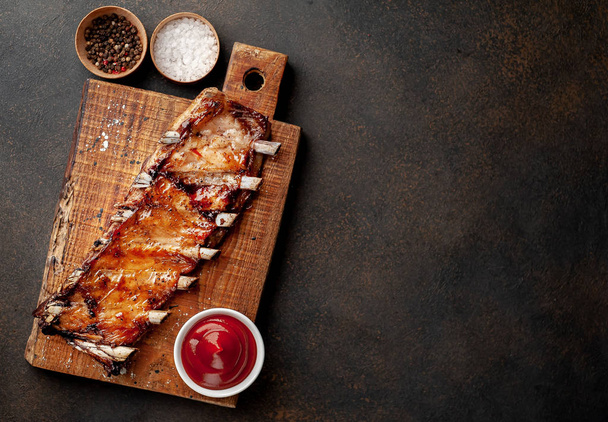 Roasted pork ribs on wooden board with salt, pepper and bbq sauce. - Photo, Image