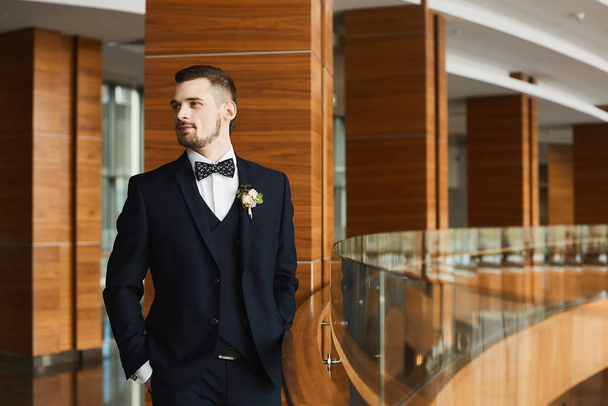 Handsome stylish bearded man in tuxedo and bow tie with a boutonniere. Young businessman in a tailored tuxedo. Beautiful groom with stylish beard in wedding suit before wedding ceremony. Male fashion. - Φωτογραφία, εικόνα