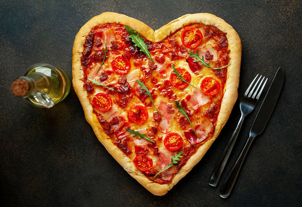 オリーブオイルとハートピザ,灰色の石の背景にフォークとナイフ.バレンタインデーのコンセプト. - 写真・画像