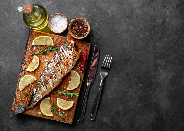 Baked mackerel with lemon and cutlery served on wooden board - Φωτογραφία, εικόνα