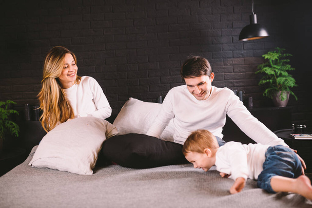 Family having funny pillow fight on bed. Parents spending free time with their son. Young family being playful at home. Happy parents and child. Young caucasian family fighting with pillows - Фото, изображение