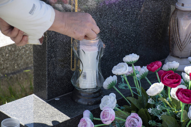 Frau auf Friedhof zündet weiße Kerze mit Streichholz am Grab an - Foto, Bild