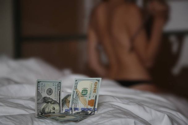 Τα χρήματα και η νεαρή γυναίκα στο δωμάτιο του ξενοδοχείου ως σύμβολο της πορνείας, της σύγχρονης δουλείας και της εμπορίας ανθρώπων. Η εμπορία ανθρώπων και η έννοια της ξενοδοχειακής βιομηχανίας. - Φωτογραφία, εικόνα