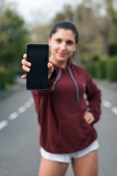Sporty young woman showing smartphone. Focus on phone screen. Fitness workout app concept. - Foto, Imagen