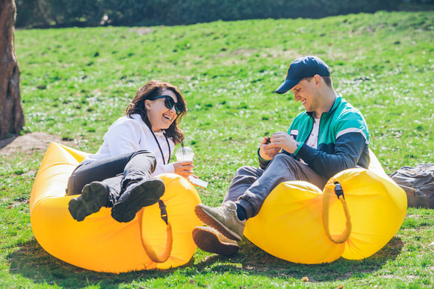 couple laying on inflatable mattress in city park at sunny day. talking and chatting - Photo, Image