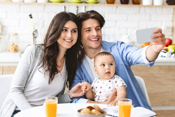 Ευτυχισμένοι γονείς που παίρνουν selfie με το μωρό στο εσωτερικό της κουζίνας - Φωτογραφία, εικόνα