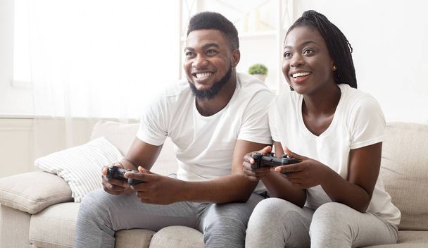 Vrolijke zwarte echtgenoten die videospelletjes spelen op een console met joysticks - Foto, afbeelding