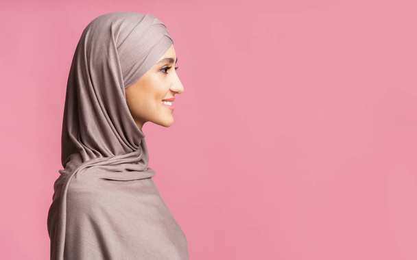 Profile portrait of beautiful arabic woman in hijab over pink background - Foto, Imagen