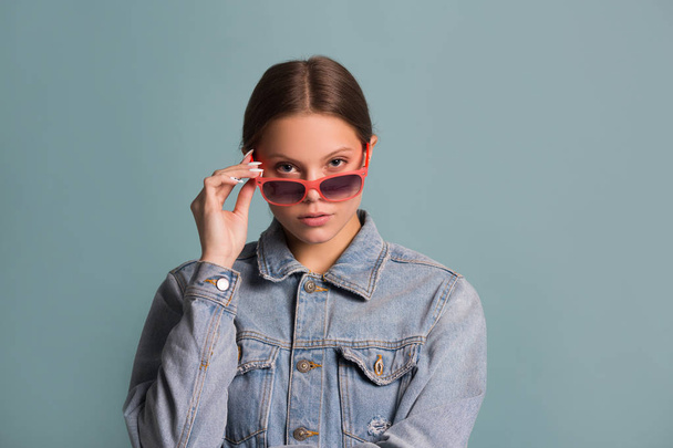 portrait of a beautiful young woman in sunglasses on a blue background - Fotografie, Obrázek